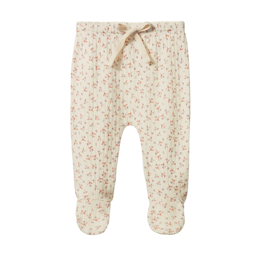 A pair of baby footed pants in a cream-colored muslin fabric with a small red and pink floral print, featuring an elastic waistband with a matching fabric drawstring.