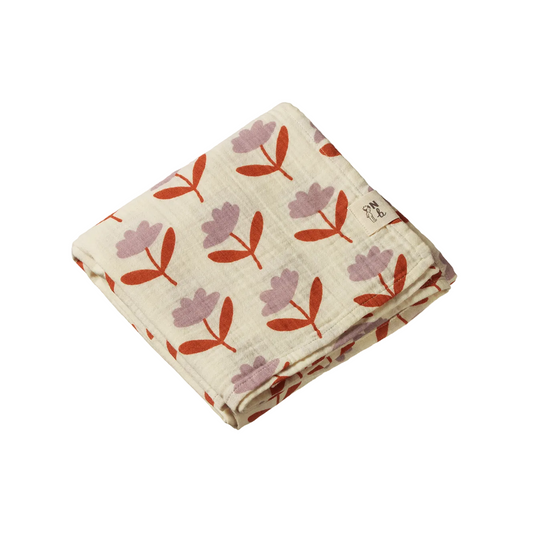 A folded muslin baby blanket with a repeating floral pattern in dusty pink and terracotta orange on a warm cream background, featuring a small woven brand tag on the side.